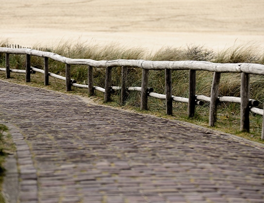 Gebogen bakstenen pad door de duinen van Texel met houten hekwerk
